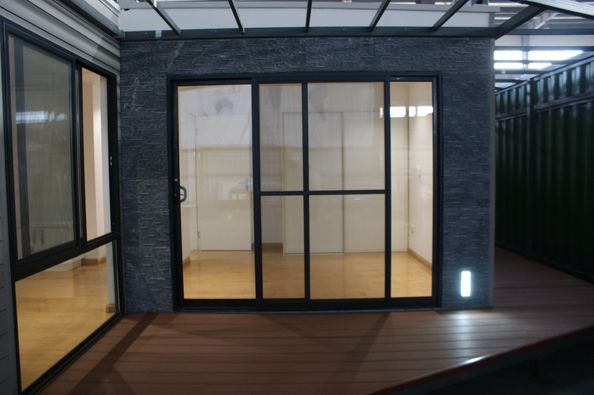 Sliding glass doors with black frames in a room with wood flooring, set against a dark, textured wall.