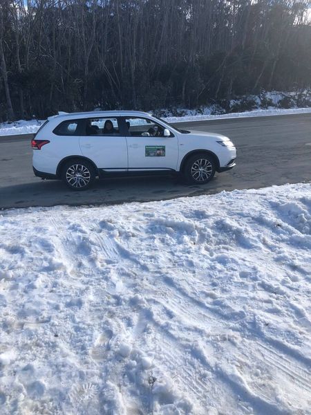 White SUV parked on a snowy road with a forest in the background.