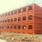 Three-story building under construction; orange shipping containers with scaffolding around windows.