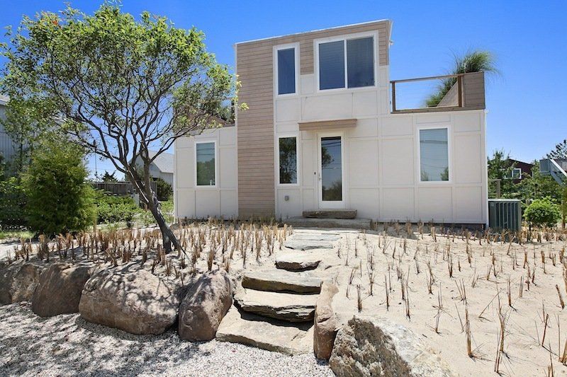 Modern two-story house with a sand-covered yard and stone steps leading to the front door.