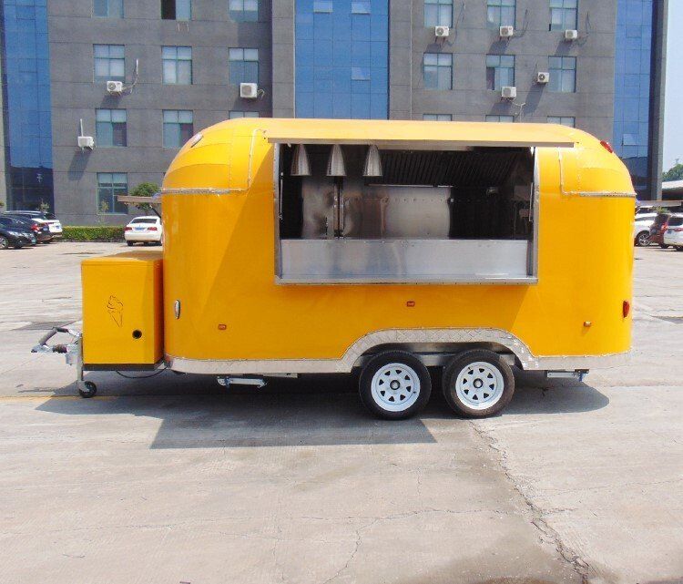 Yellow food truck parked in front of a building with a serving window open, on a sunny day.