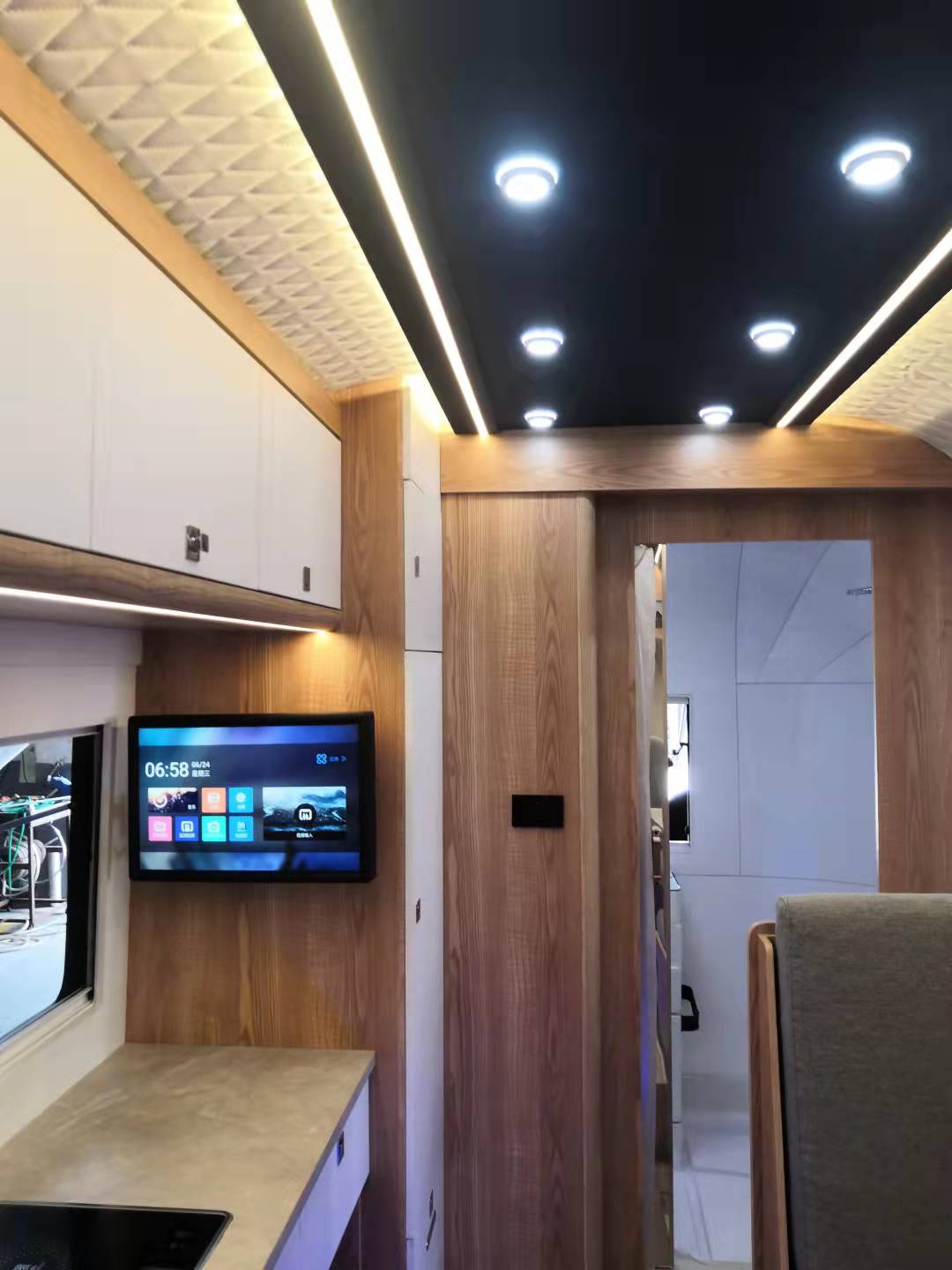 Interior of a motorhome with a TV, cabinets, and a doorway to another room. Brown wood paneling and white trim.