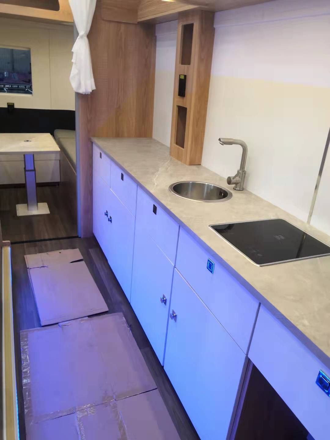 Interior view of RV kitchen with white cabinets, light countertop, sink, and stovetop.