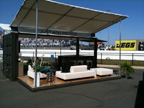 Outdoor lounge built from a shipping container, with seating, a bar, and a roof, at a racetrack.