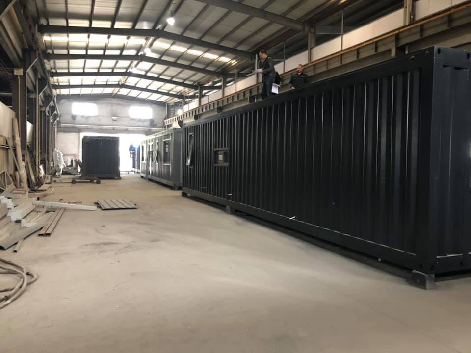 Shipping containers inside a warehouse. Workers are on top of one container.