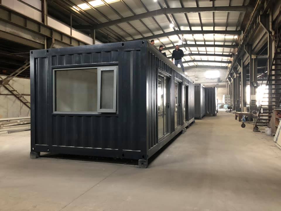 Dark grey container building with windows inside a large warehouse.