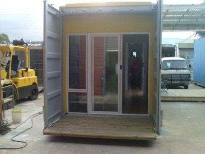 A shipping container converted into a structure with sliding glass doors, a wooden deck, and a yellow interior.