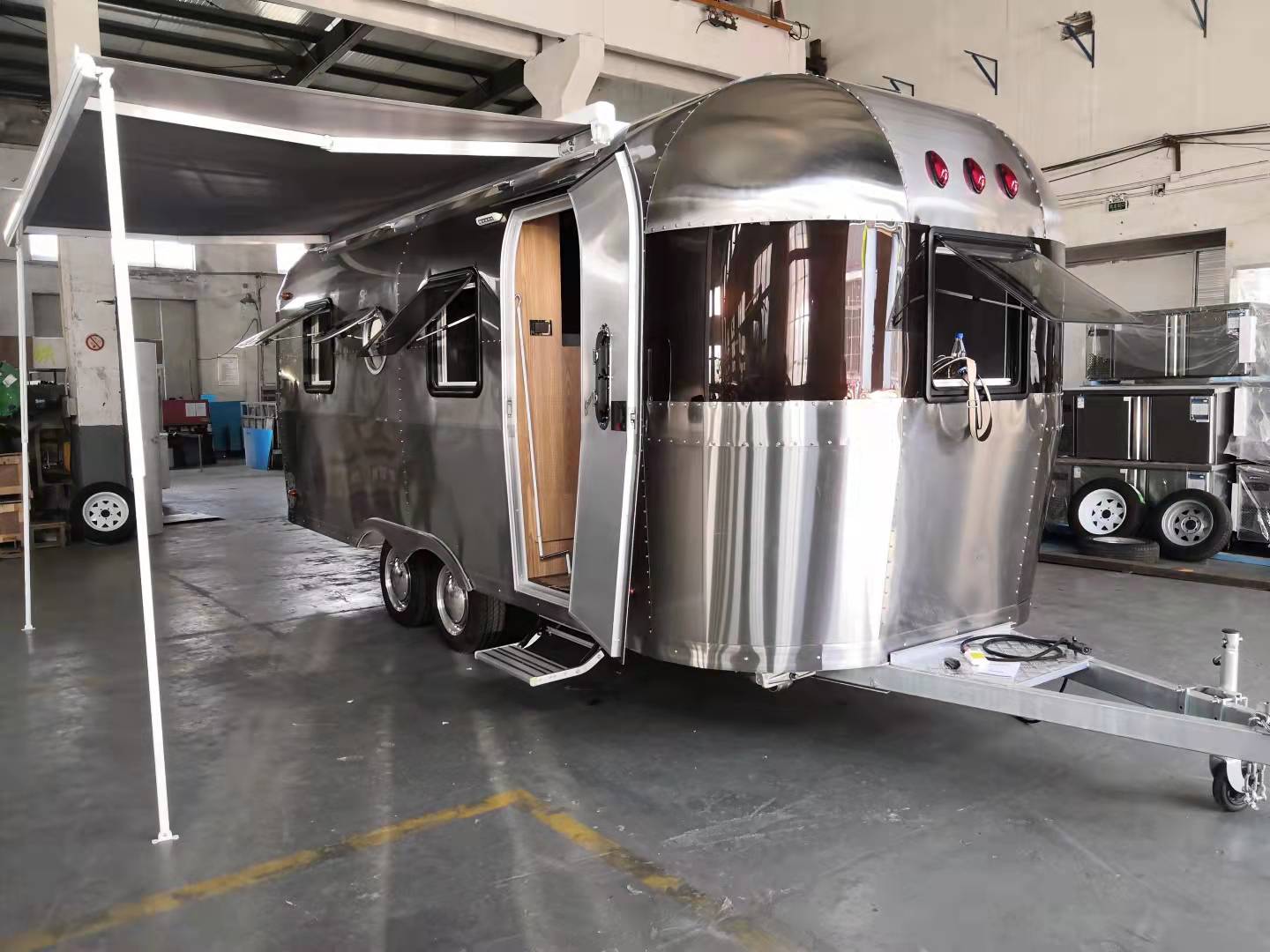 Shiny silver camper trailer with awning extended, door open, parked indoors.