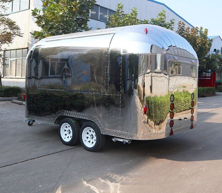 Shiny silver food trailer with rounded edges, two wheels, parked on pavement.