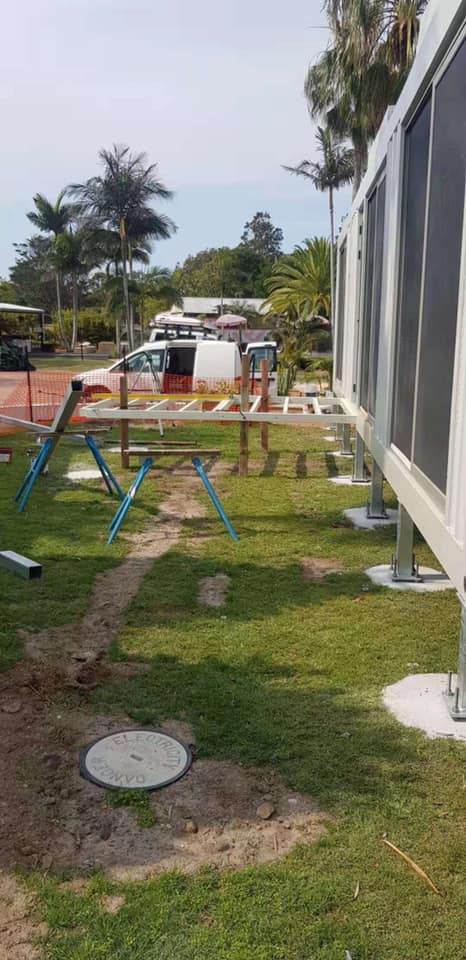 Construction site with a white van, green grass, and ladders. Grey container on the right.