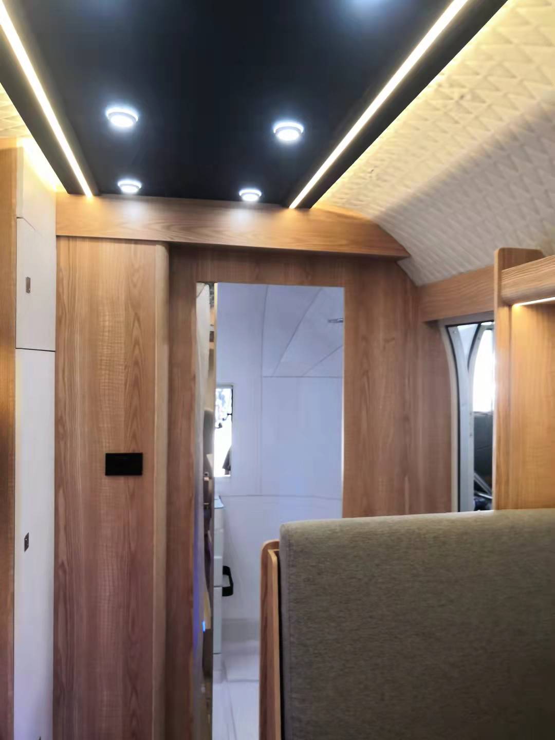 Interior of a modern RV with light wood paneling, sliding door, and recessed lighting.