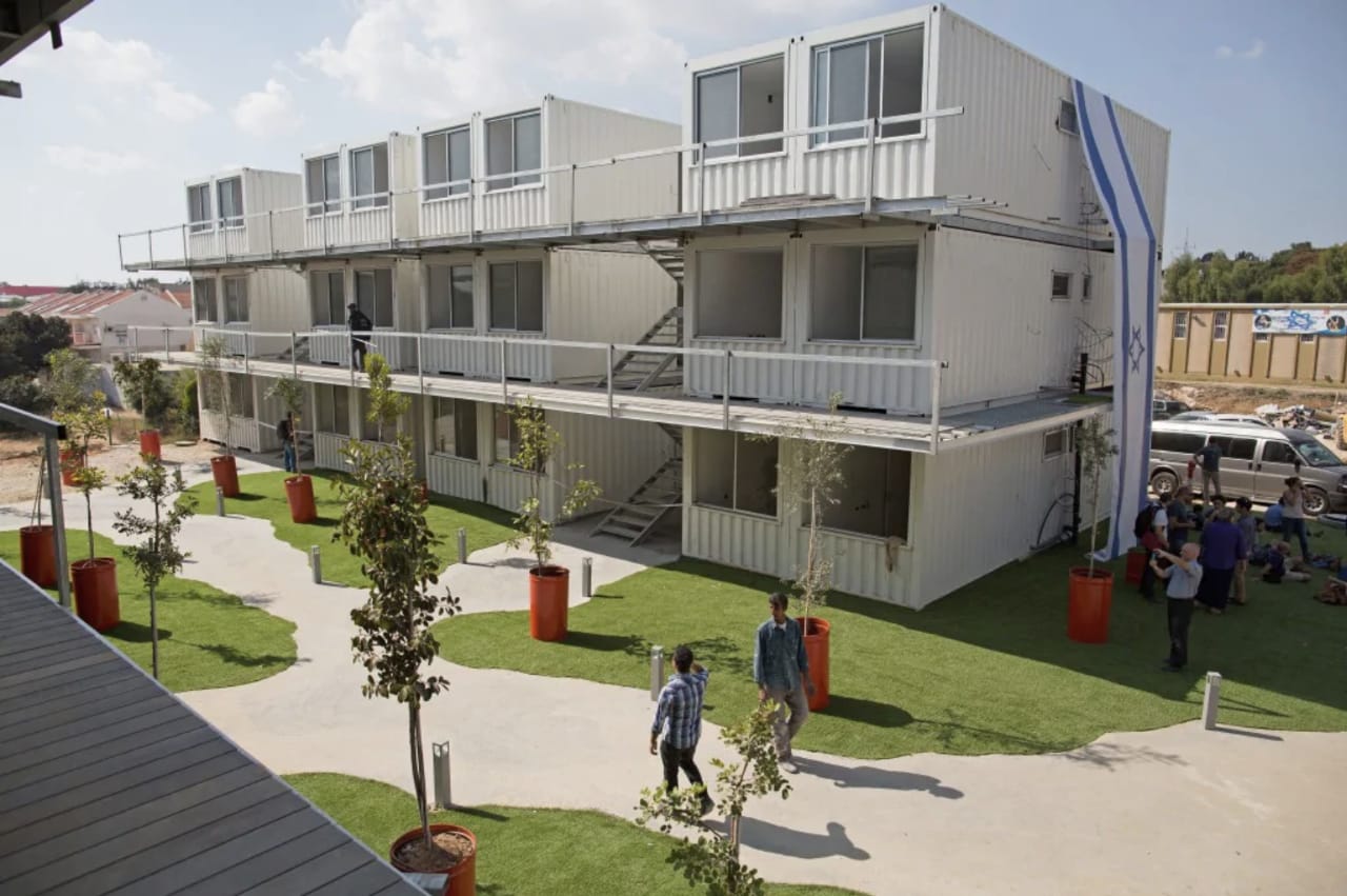 Multi-story building constructed from shipping containers with exterior staircases, greenery and people.