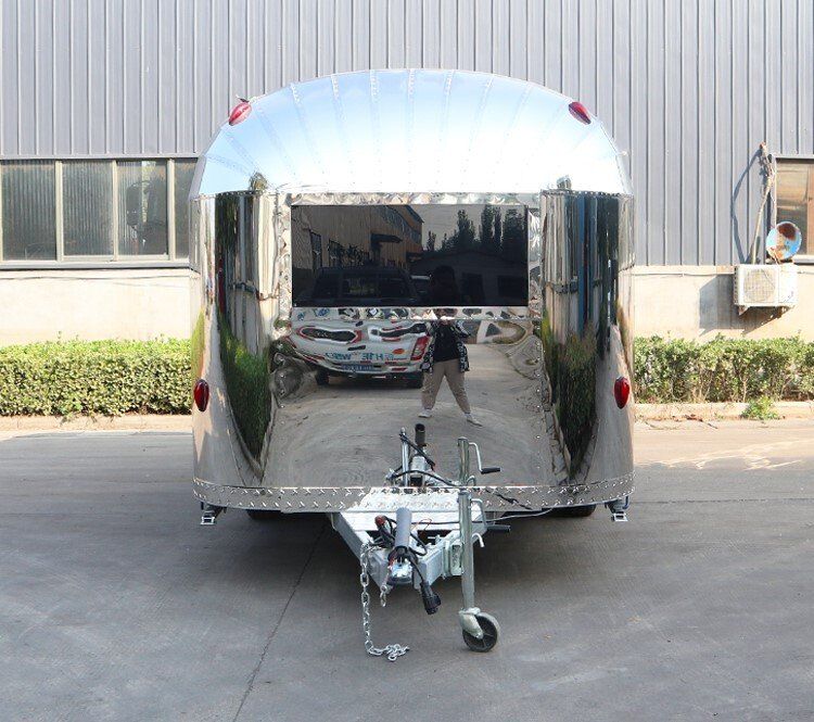 Shiny, silver food trailer with open serving windows, hitch, and lights.