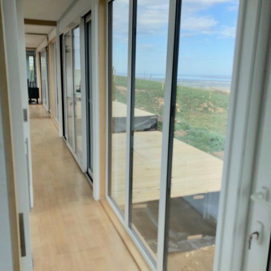 Interior view of a hallway with glass doors, wooden flooring, and a coastal view.
