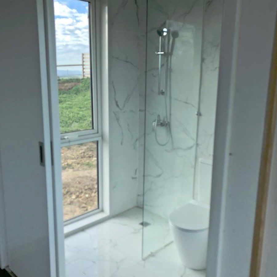 Bathroom with white marble tile, glass shower, window, and toilet.