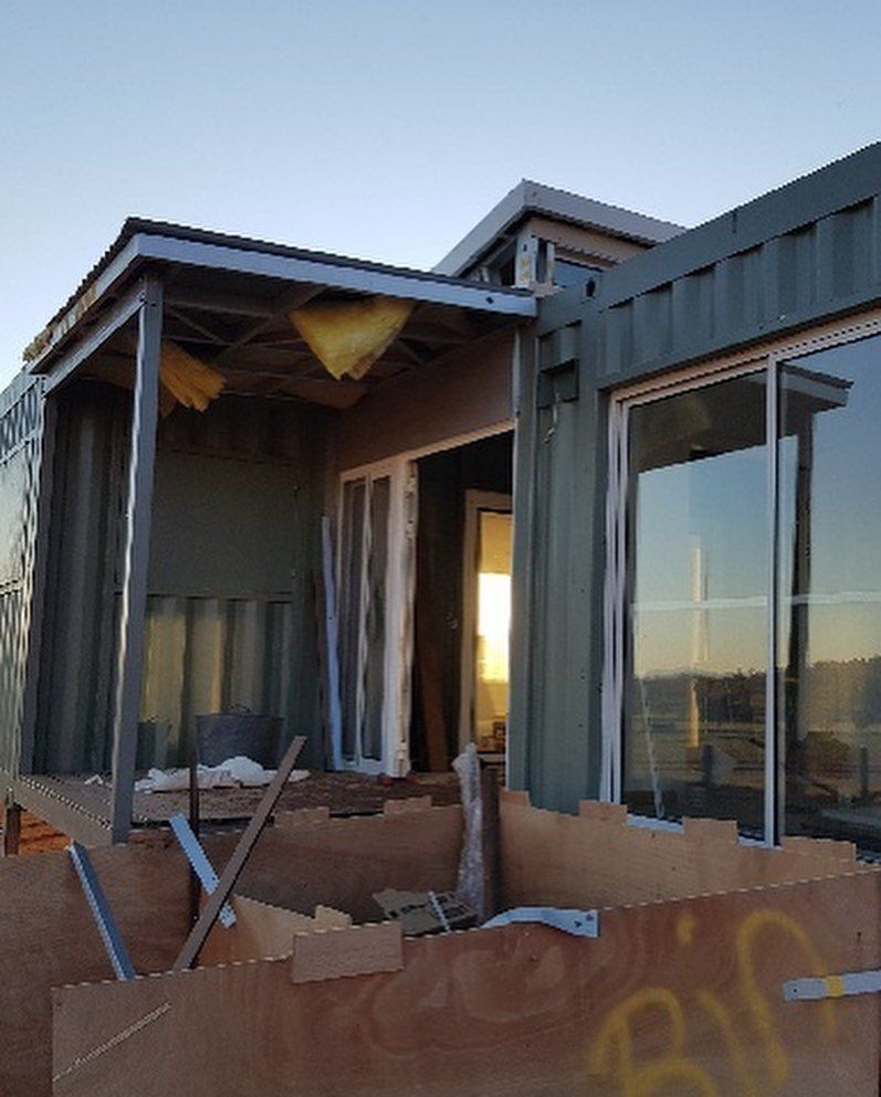 Shipping container home under construction, with a covered porch and large windows.