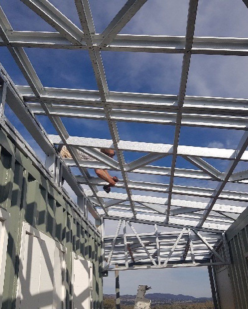 Metal framework of a roof under construction against a blue sky with visible beams.