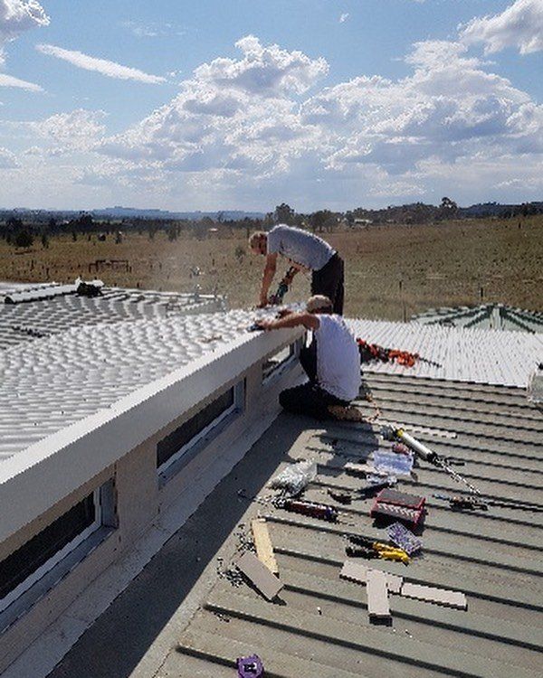 Two people on a roof working, installing a white structure. Sunny day with tools visible.