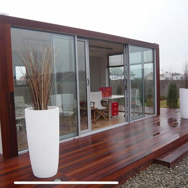 Modern building with glass sliding doors, wooden deck, and tall white planters. Overcast day.