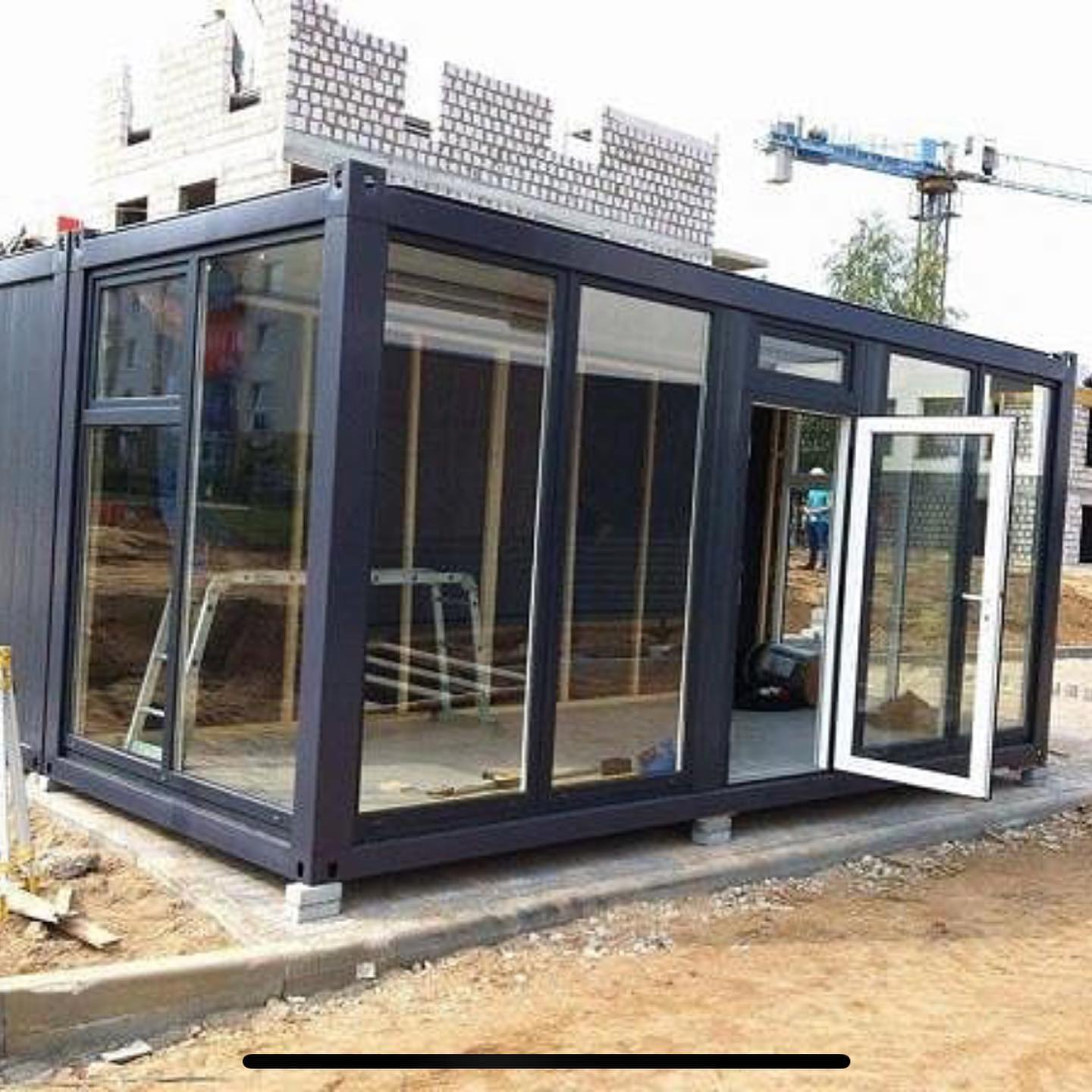 Black and glass modern structure, possibly a home, under construction with an open door.