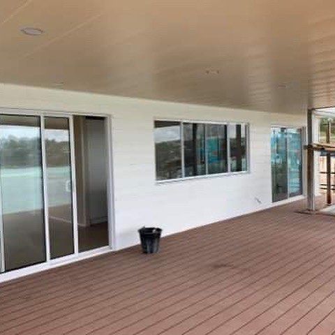 Exterior of a home with brown deck, white siding, and sliding glass doors.