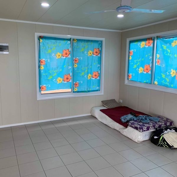 Interior room with tiled floor, two windows with blue curtains, and a mattress.