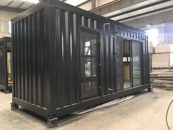 Black container home with glass doors in a warehouse.
