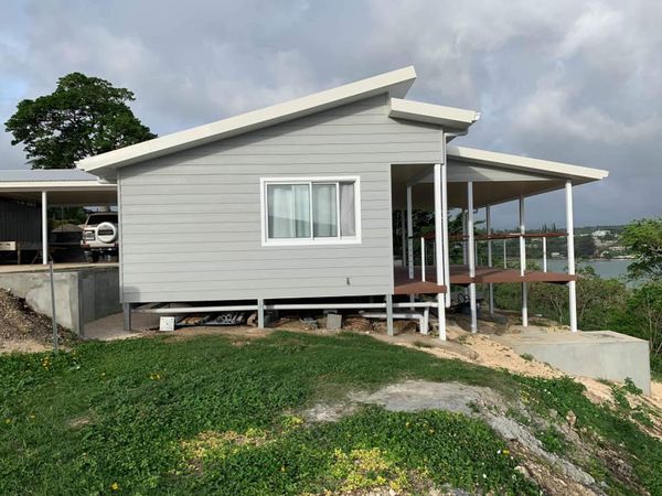 Light gray beach house with covered deck and white trim, set on a grassy hill overlooking water.