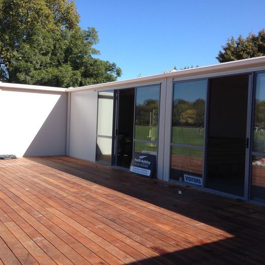 Wooden deck outside a modern building with large glass doors reflecting a sunny outdoor scene.