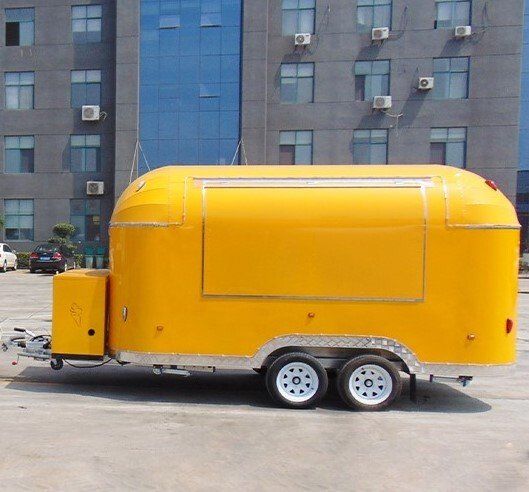 Yellow food truck trailer with service window, two wheels, parked outdoors.