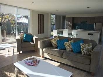 Spacious living room with sofa, armchair, coffee table, and open kitchen with a sunny window view.