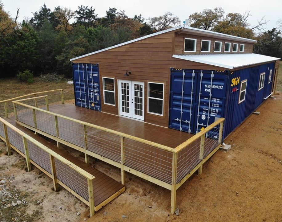 Container home with wooden deck and ramp. Blue containers, brown siding, and white roof.