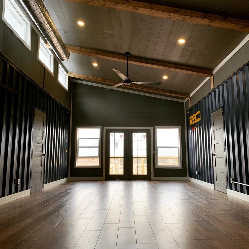 Empty room with wood floors, dark walls, windows, and exposed wooden beams.