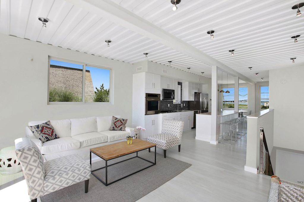 Bright, modern living room with white walls, a sofa, and kitchen in the background.