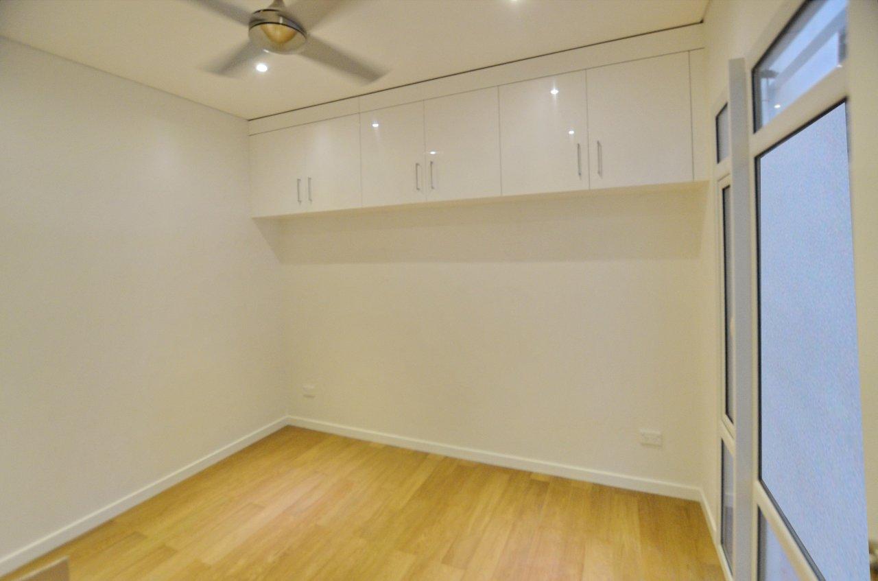 Empty room with light wood floors, white walls, and overhead storage cabinets. Doorway on right.