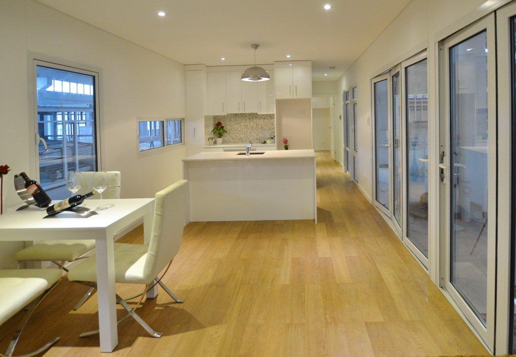 Modern white kitchen/dining area with wood floors, island, table, and sliding glass doors.