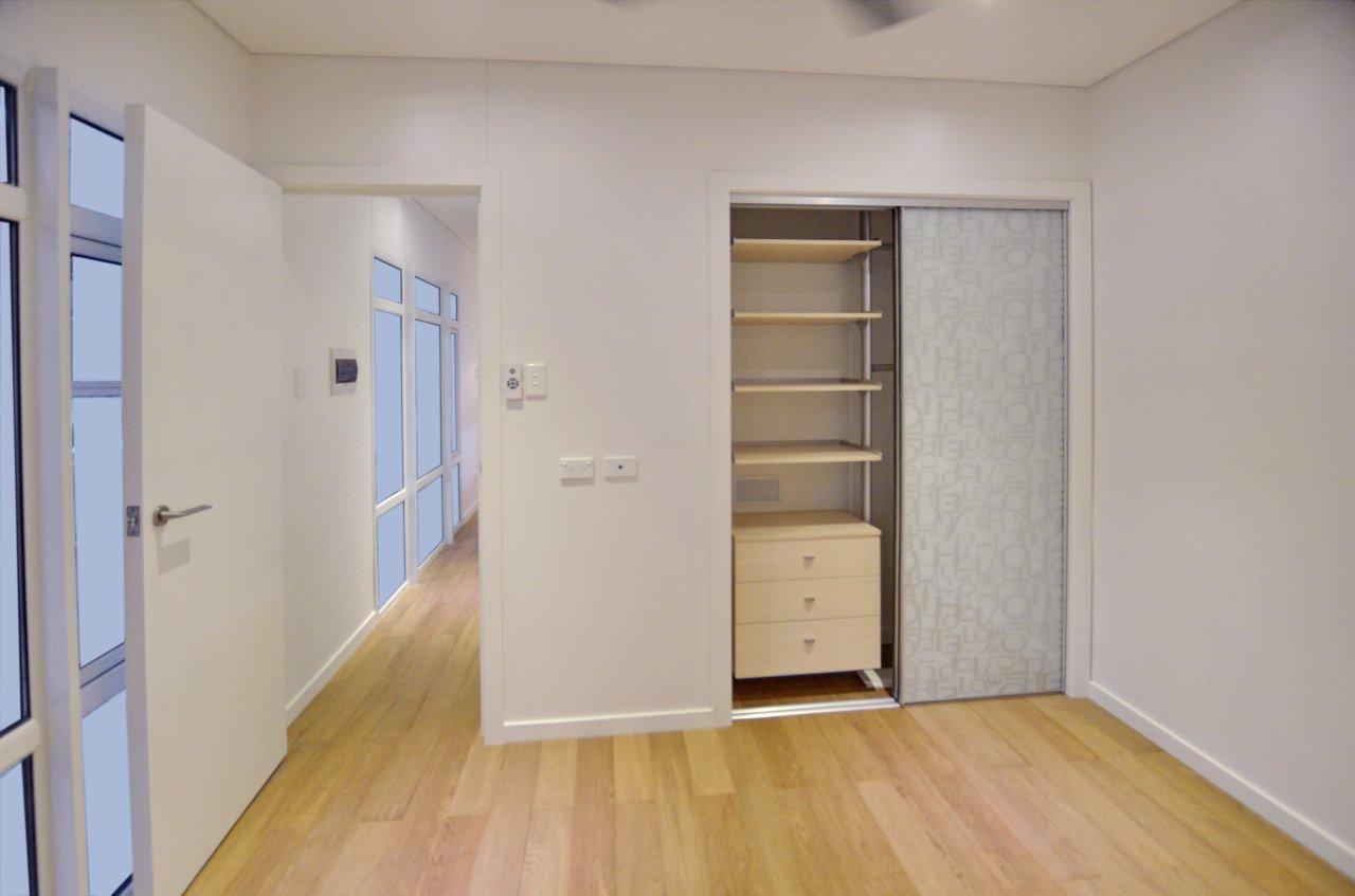 Empty room with wood floors, closet, and a hallway leading to glass panel doors.