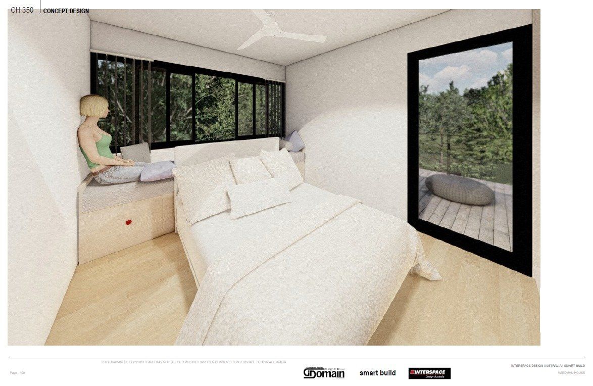 Bedroom interior with a large bed, windows, and a person sitting by a window using a laptop.