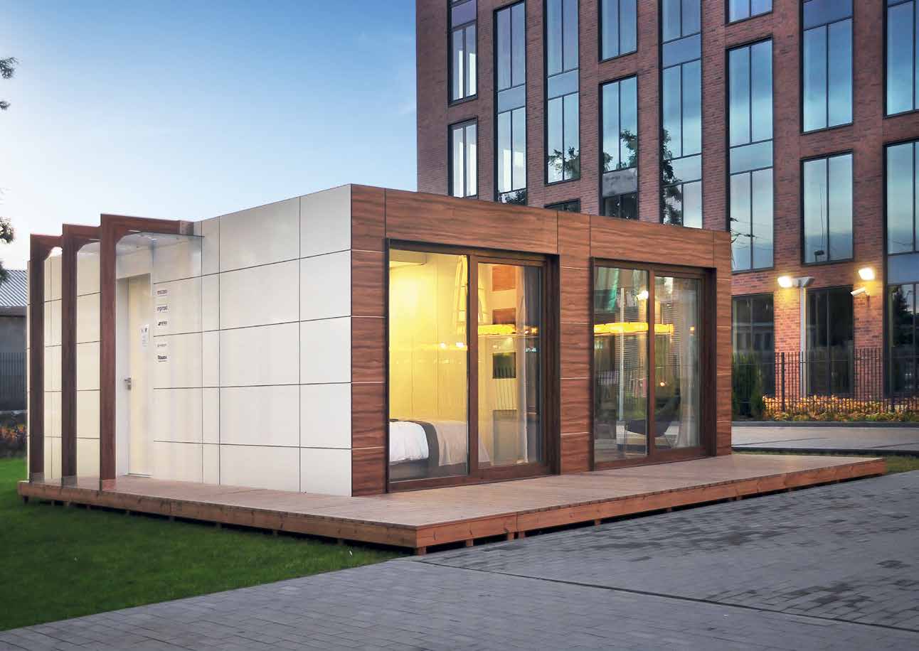 Modular, modern small building with wood and white paneling, glass doors, and a wood deck.