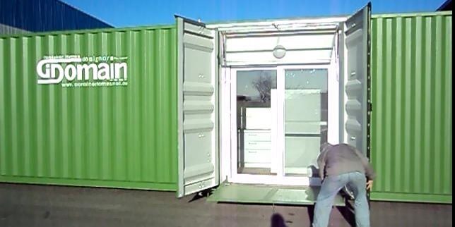 Man entering converted shipping container with a glass door, green exterior, sunny day.