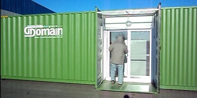 A person entering a green shipping container office. The container has a glass door with the company's logo.