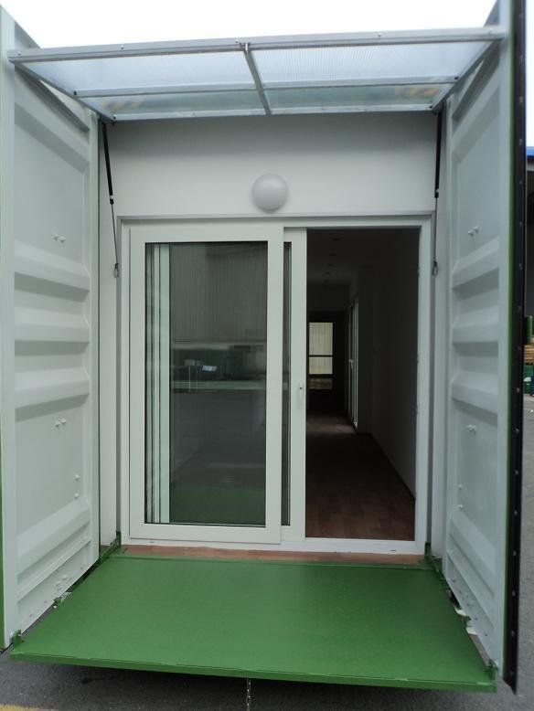 Shipping container converted into a small structure, with doors and a glass sliding door, green floor, and partial roof.