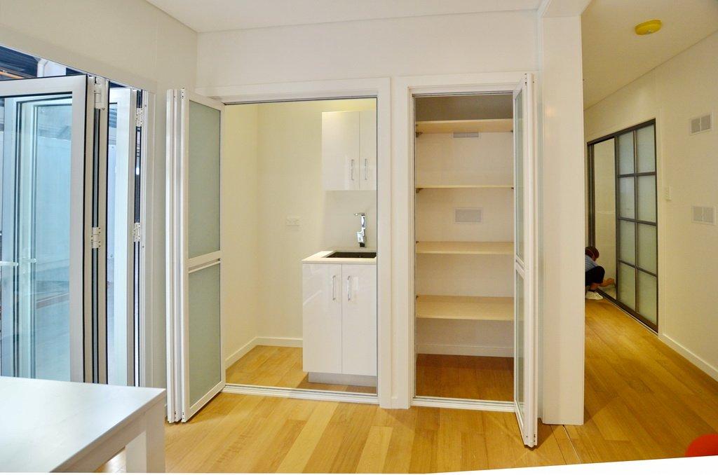 Interior with white cabinets, shelving, and sink in a small room with bi-fold doors, wooden floor.
