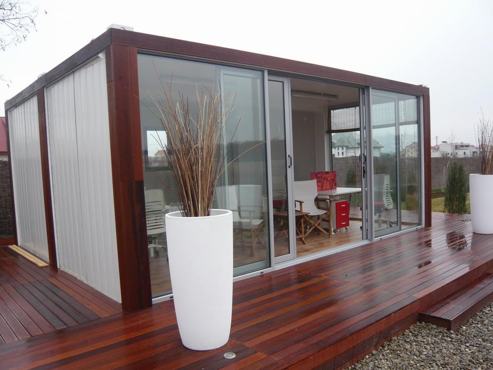 Modern cabin with wood deck and large glass sliding doors, featuring a potted plant.
