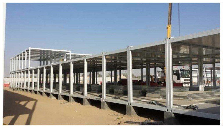 Steel frame building under construction in a desert environment; crane is visible.