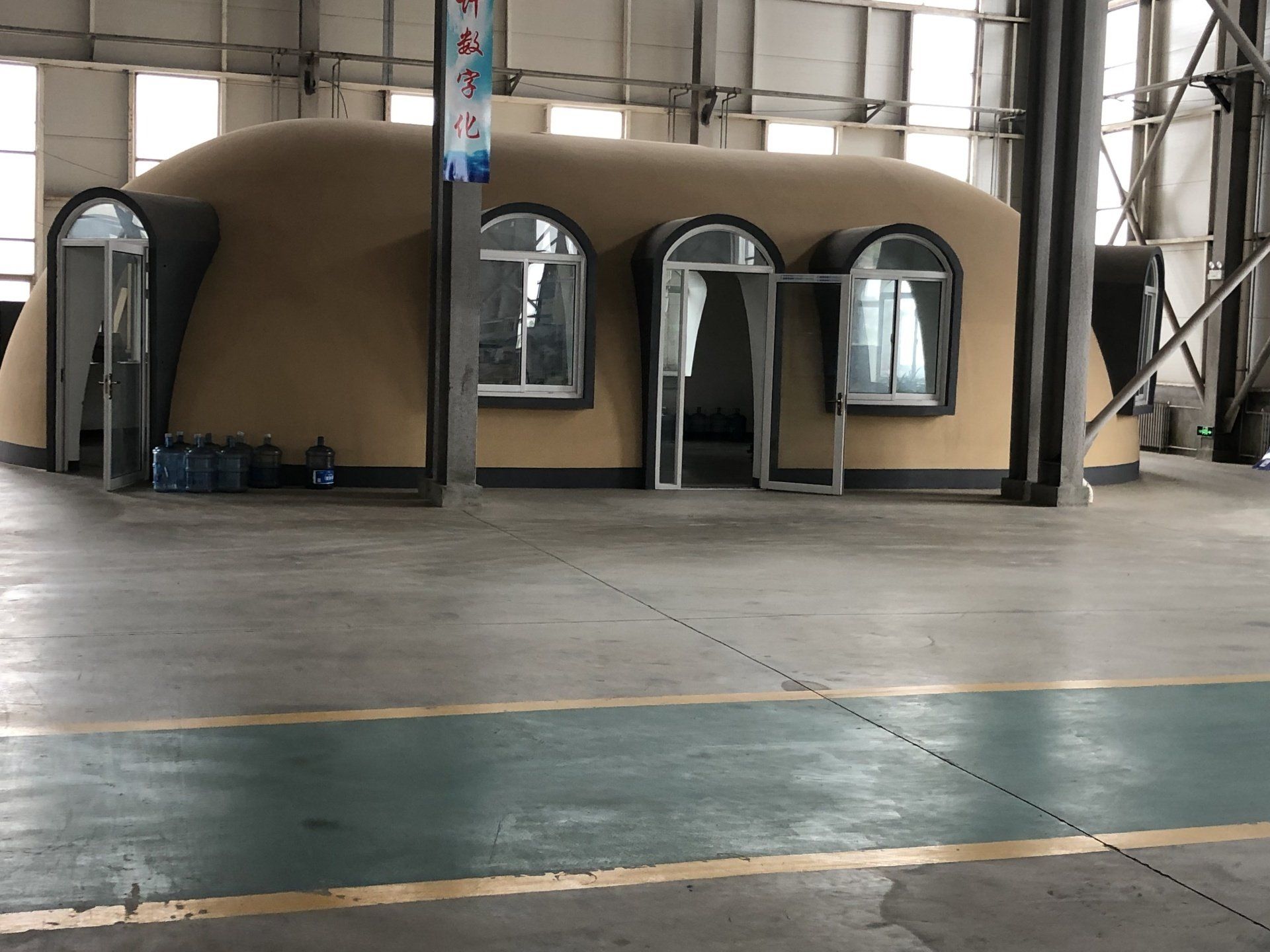 A tan-colored, dome-shaped building inside a large industrial space with windows and doors.