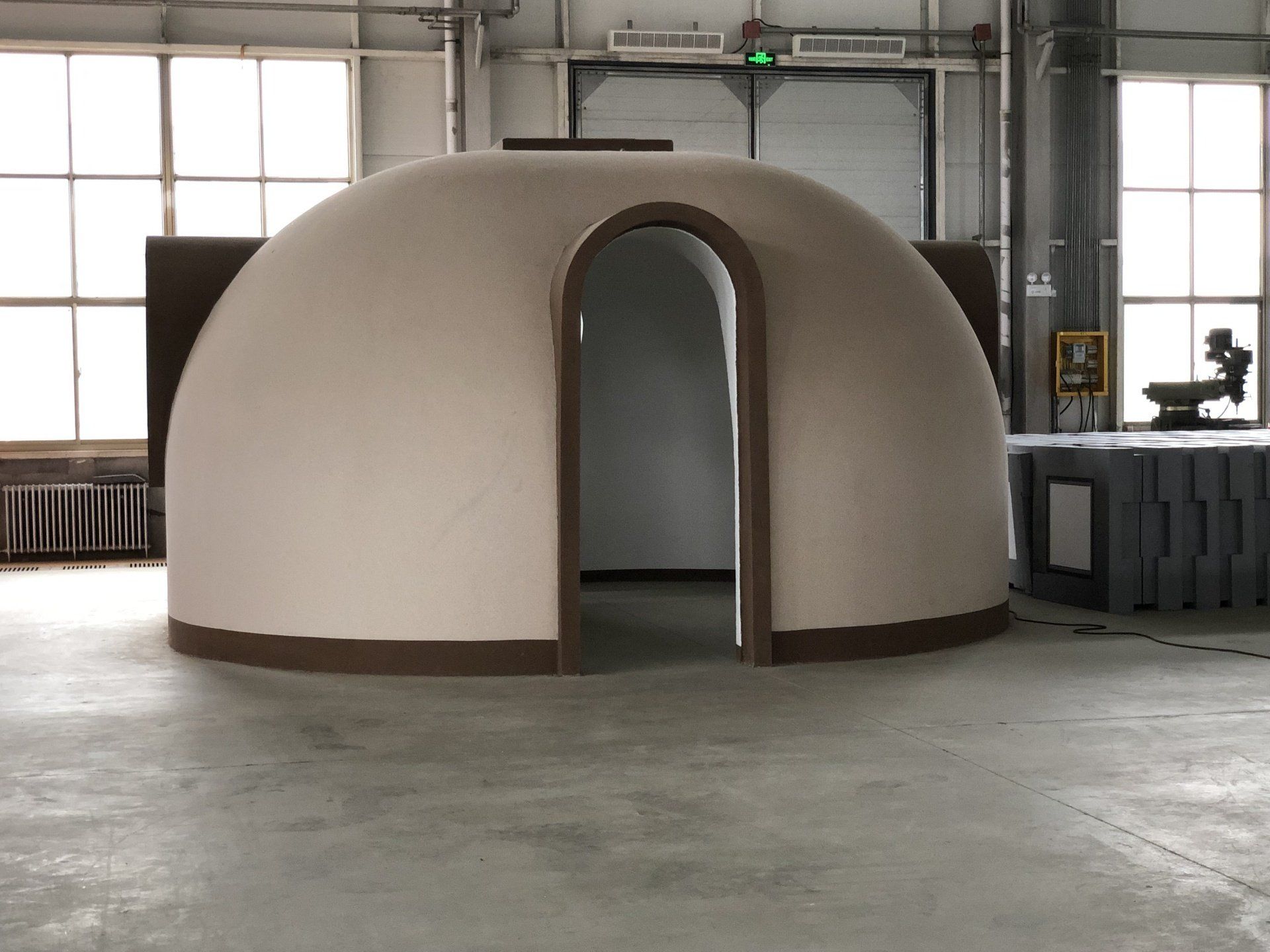 Beige dome-shaped structure with an arched doorway inside a warehouse.