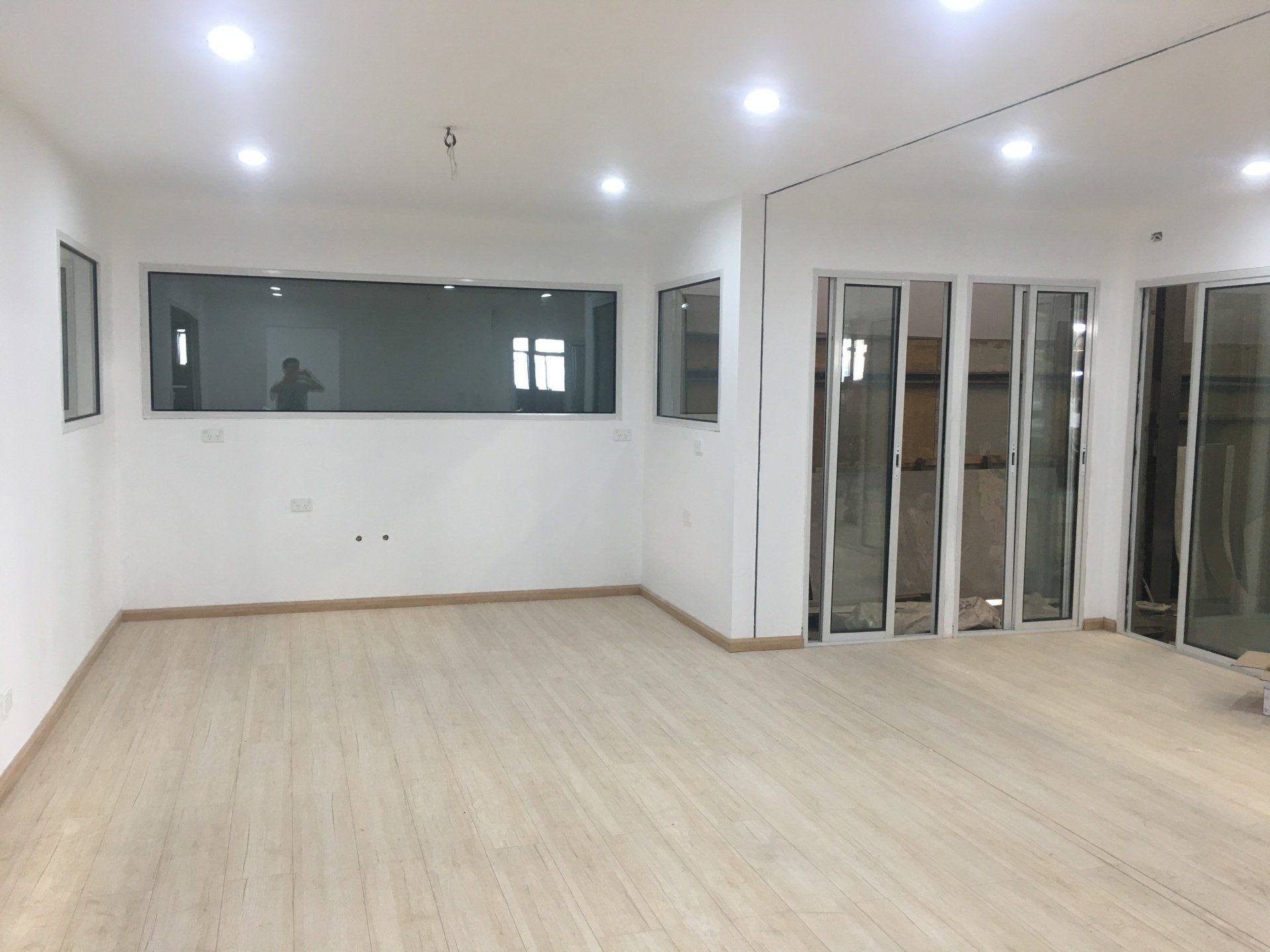 Empty office space with light wood flooring, white walls, large windows, and recessed lighting.