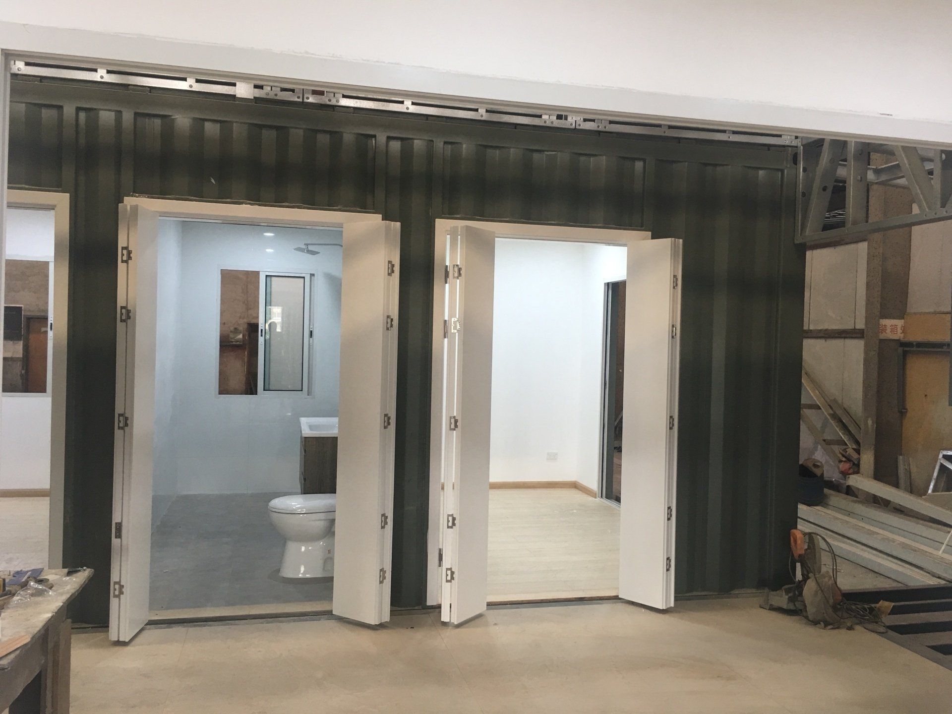 Interior construction view with container wall, doorways leading to a bathroom and another room.
