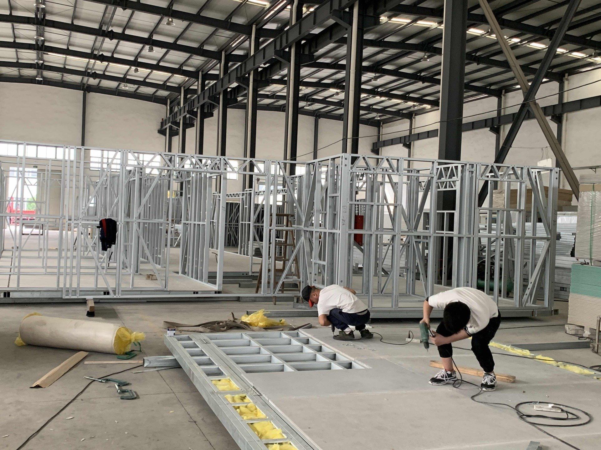 Construction workers assembling metal framework inside a large warehouse.